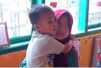 Foto : Nuraeni saat (9) menggendong adiknya saat belajar di sekolah